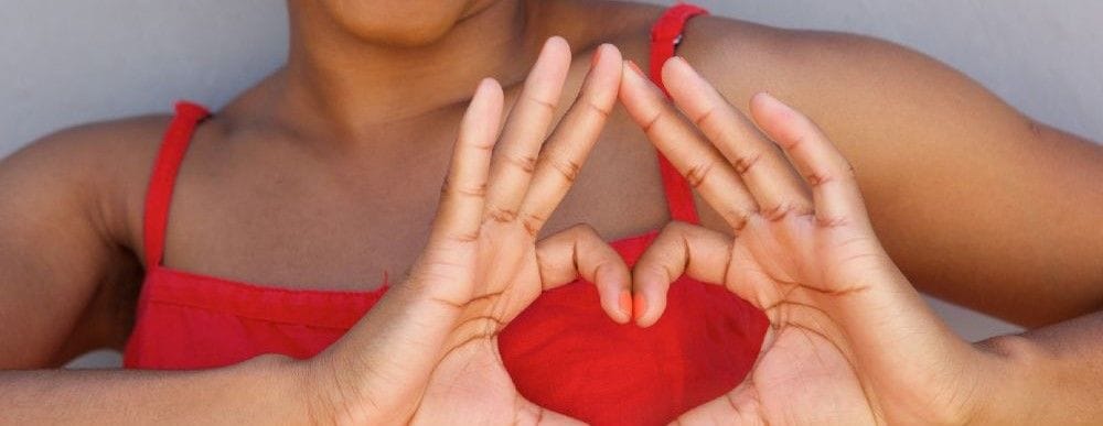 Close-up of a woman in a red dress forming a heart shape with her hands, symbolizing love and positivity